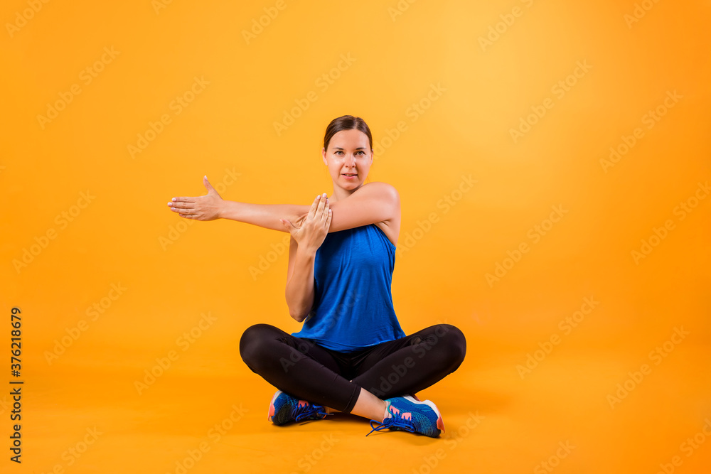 A brunette woman in a sports uniform does a stretch on an orange background A brunette woman in a sports uniform does a stretch on an orange background