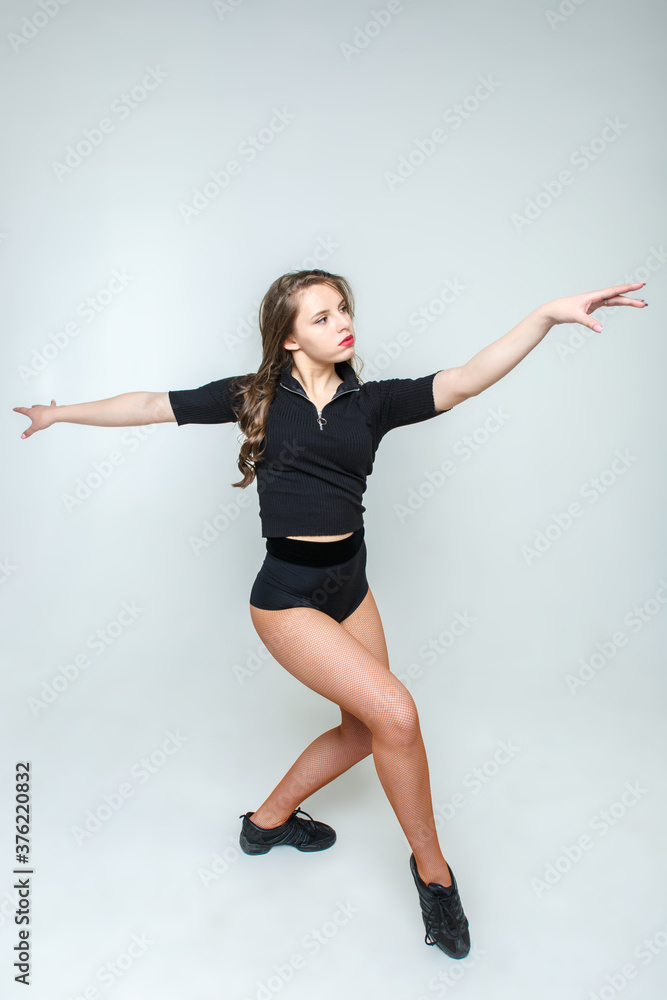 A young and beautiful woman with long wavy hair posing in full growth in front of the camera on a light background. The girl stands in a pose imitating a dance.