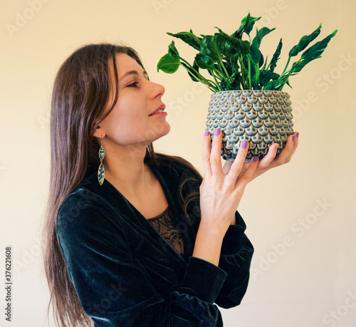 Beautiful young woman in a boho style outfit with a unique variety of a climbing plant - Epipremnum 'Green Javelin' ('Godzilla') with twisted leaves in a designer pot with a scale pattern photo