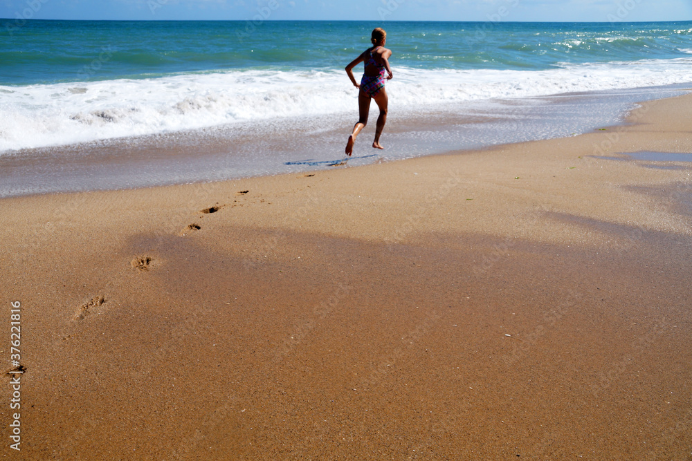 teenage girl runs along the seashore, leaving footprints on the wet sand teenage girl runs along the seashore, leaving footprints on the wet sand
