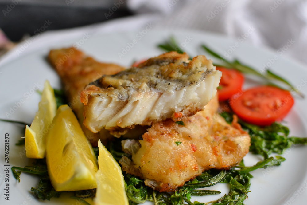 Fried fish fillet with tomatoes, lemon and rosemary. White plate. Light background. Close-up.