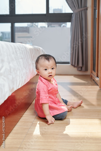 Curious adorable little girl in pink shirt crawling on the floor and exploring apartment