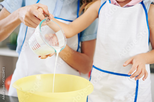 Close-up image of mother and daughter pouring fresh cold cream in bowl when making sweet frosting photo