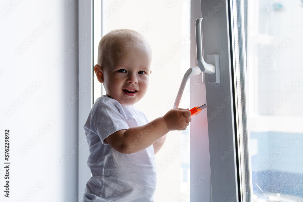 A child at an open window. A small child is in danger. Boy on the windowsill. Repair of windows. A child at an open window. A small child is in danger. Boy on the windowsill. Repair of windows.