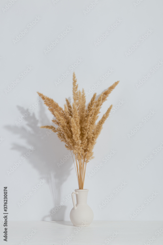 Plakat A vase with yellow spikelets on the table, on a white background. Light stylish design.
