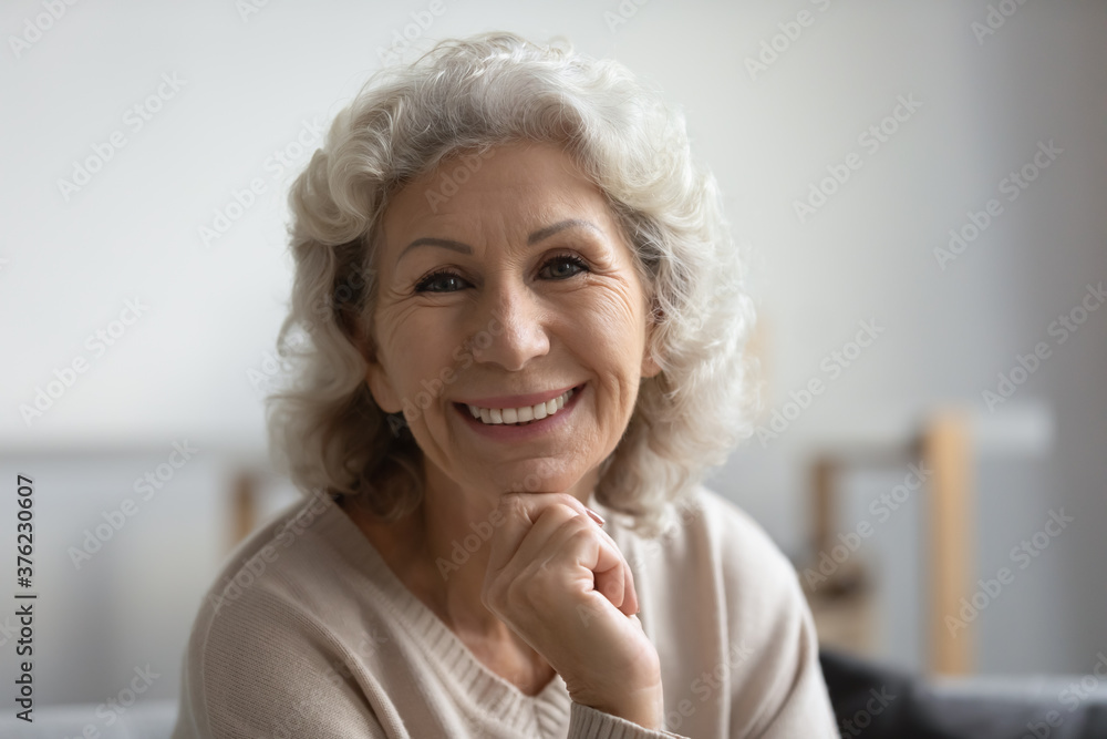 Close up head shot portrait happy beautiful mature middle aged woman with healthy toothy smile looking at camera, sitting on cozy sofa at home, posing for photo, natural beauty and skincare Close up head shot portrait happy beautiful mature middle aged woman with healthy toothy smile looking at camera, sitting on cozy sofa at home, posing for photo, natural beauty and skincare