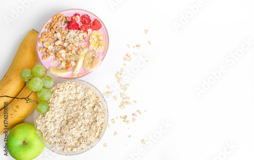 Yogurt with muesli and raspberries. Oatmeal is scattered on the table, ripe banana, nuts, apple, grapes on a white table. copy space. The concept of healthy food, diet, healthy breakfast.  © Татьяна Григорьева