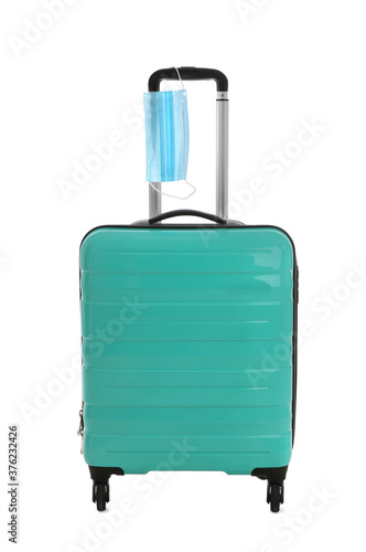 Stylish turquoise suitcase and protective mask on white background. Travelling during coronavirus pandemic