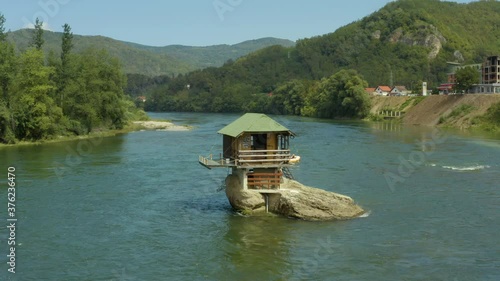 Aerial shot Serbia. Drone video in which a small house stands on a rock in the middle of the river where you can see the rocks, water, forest and trees, and the landscape. On a background of beautiful