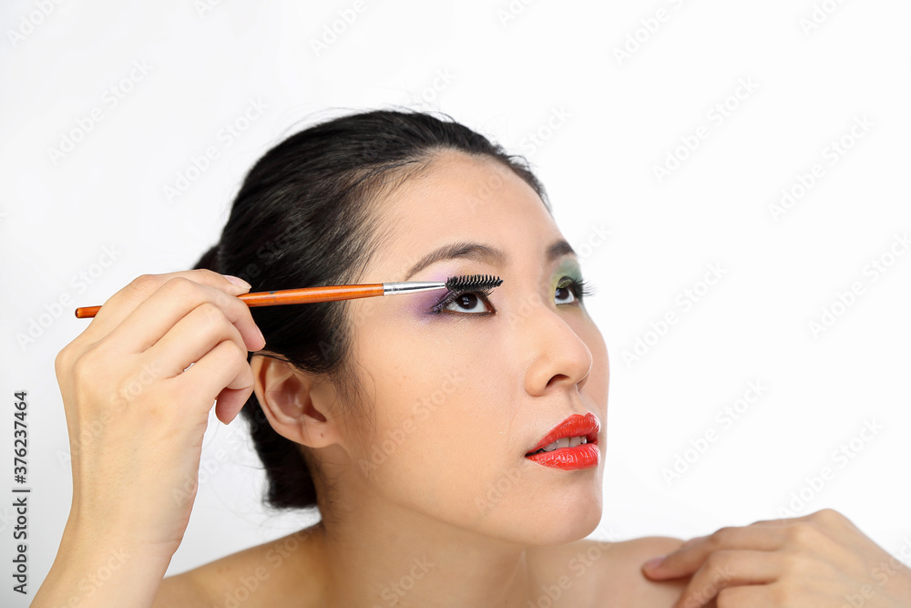 young beautiful Southeast Asian woman beauty fashion makeup light grey white background putting on eye shadow with makeup brush