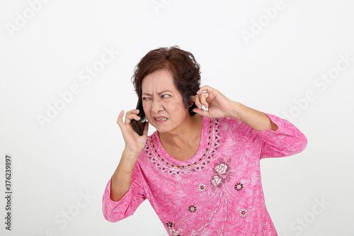 Elderly asian Chinese female on white background talking on phone can not hear face expression finger in other ear