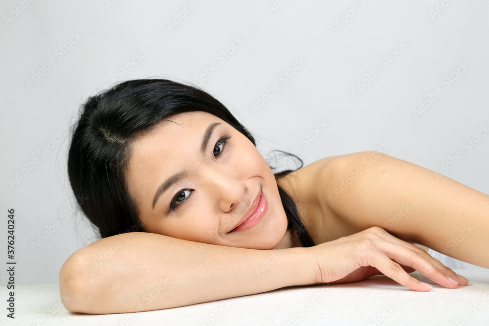 Young beautiful Southeast Asian woman beauty fashion makeup light grey white background laying on her hand smile at camera Young beautiful Southeast Asian woman beauty fashion makeup light grey white background laying on her hand smile at camera