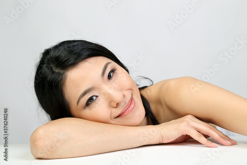Young beautiful Southeast Asian woman beauty fashion makeup light grey white background laying on her hand smile at camera