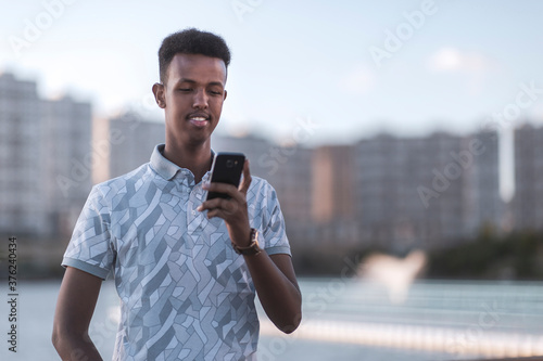 Young black man in casual clothes typing a sms with his mobile phone, copy space includes photo