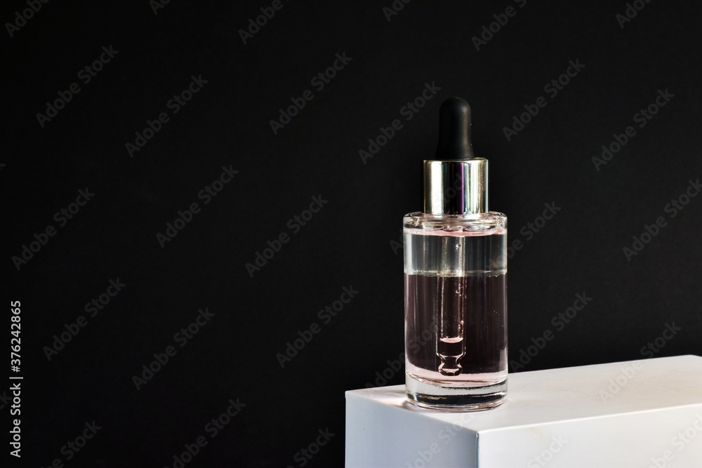 Bottle of moisturizing face oil on a white stand on a black background. A professional product for the perfect complexion. Women's accessories, beauty base. Copy space. Bottle of moisturizing face oil on a white stand on a black background. A professional product for the perfect complexion. Women's accessories, beauty base. Copy space.