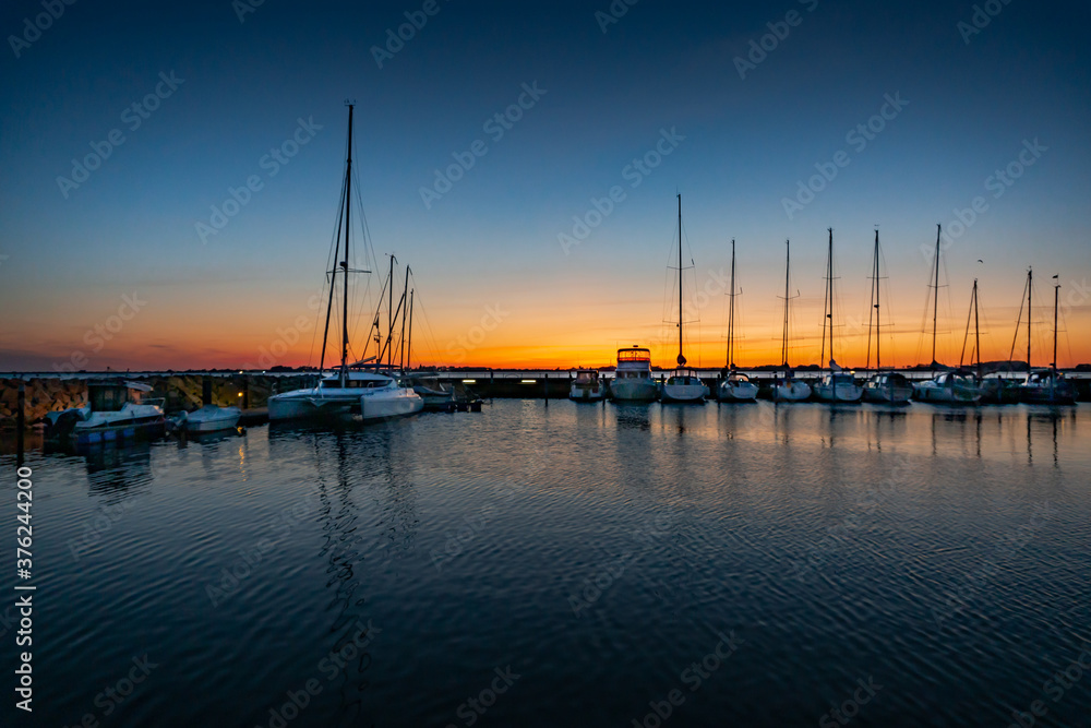 Beautiful sunset of a harbour with reflections in calm water with sailing boats and motor yachts