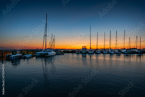 Beautiful sunset of a harbour with reflections in calm water with sailing boats and motor yachts