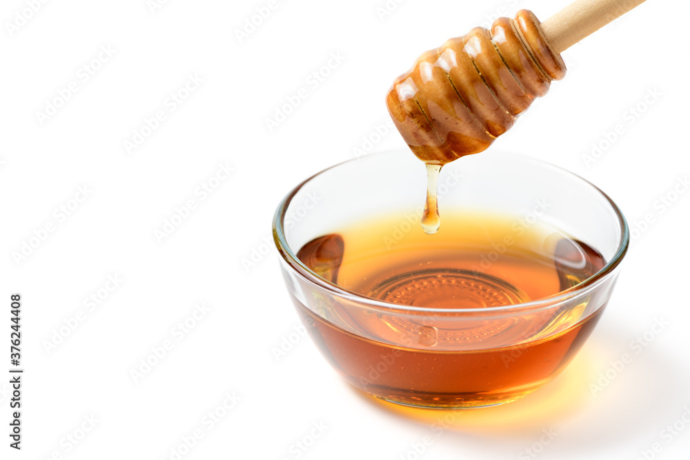 Honey is dripping from the dipper into the glass bowl isolated Honey is dripping from the dipper into the glass bowl isolated