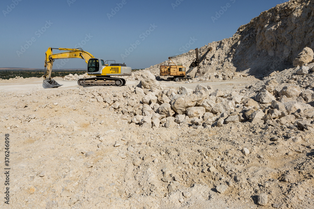 A large yellow tracked excavator is mining rock in a quarry. A large yellow tracked excavator is mining rock in a quarry.
