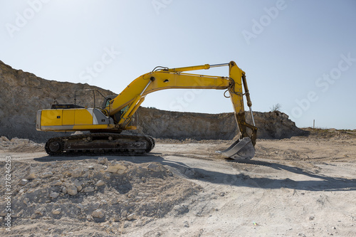 A large yellow tracked excavator is mining rock in a quarry.