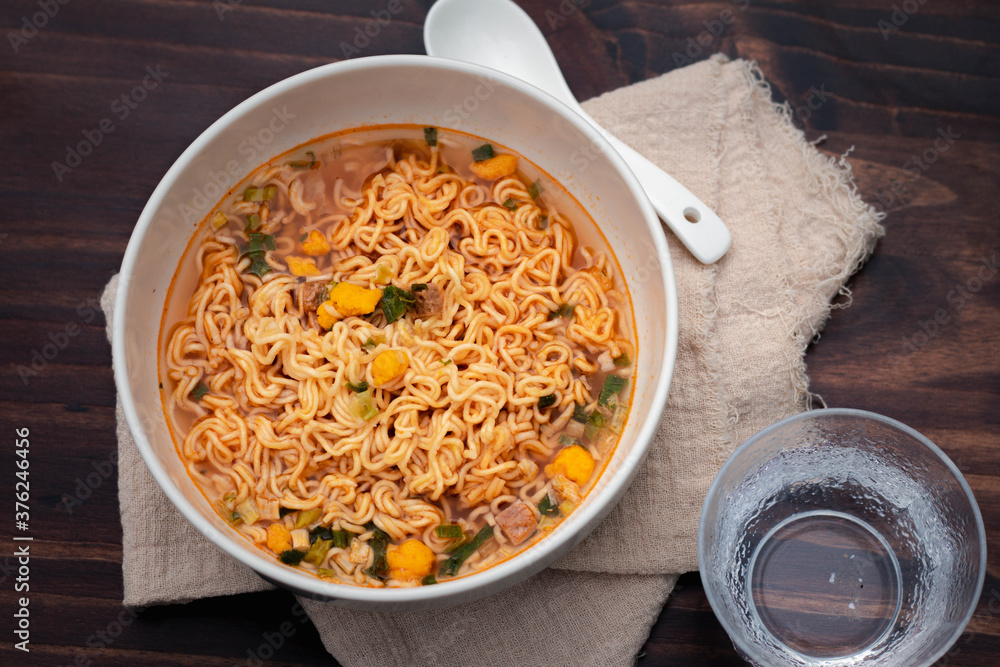 Tom Yum instant noodles in a white ceramic cup on a wooden floor