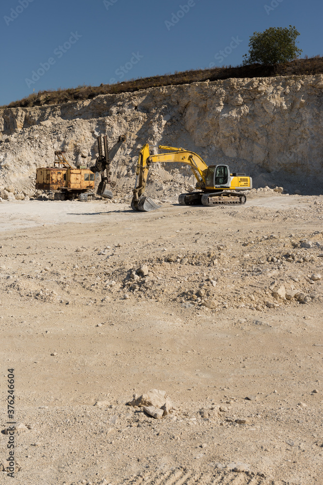 A large yellow tracked excavator is mining rock in a quarry. A large yellow tracked excavator is mining rock in a quarry.