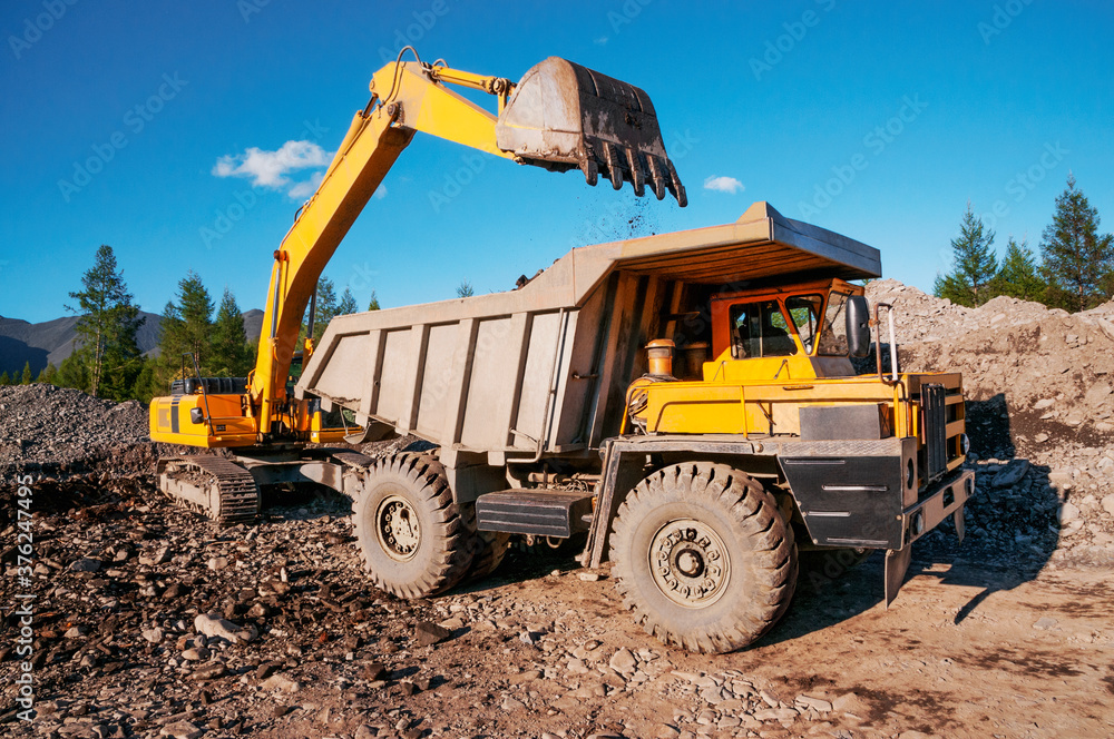 Mining dump truck in the highlands. The excavator loads the mountain soil with a bucket into the body of a dump truck Mining dump truck in the highlands. The excavator loads the mountain soil with a bucket into the body of a dump truck
