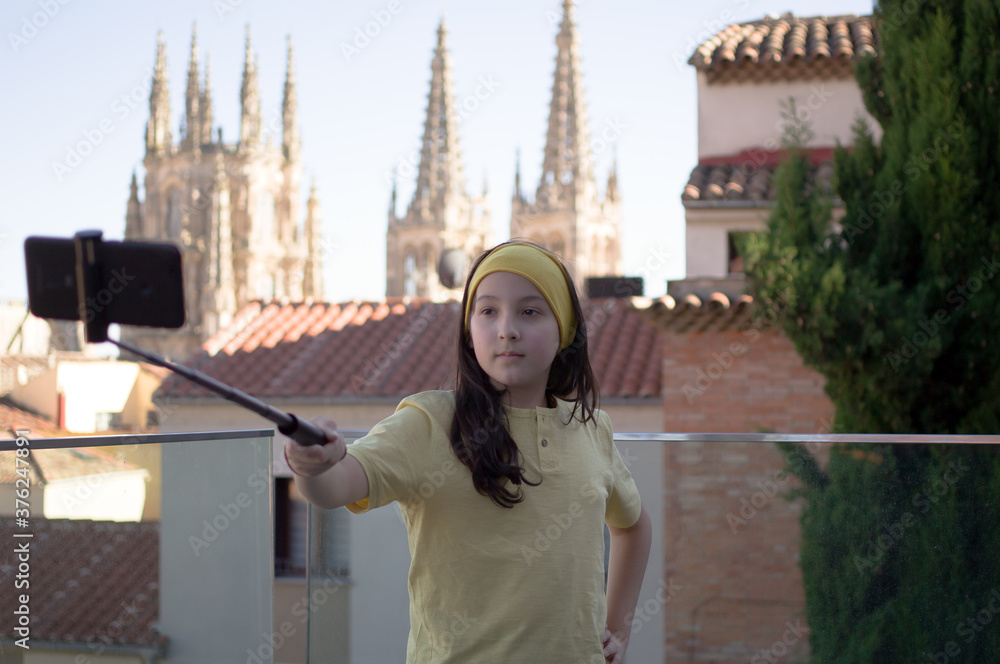 A teenager takes a selfie with a selfie stick and a gothic cathedral in the background.