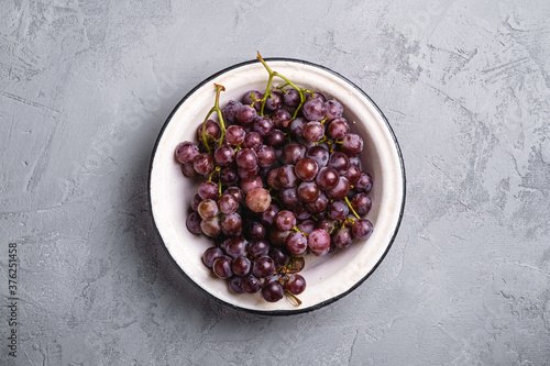 Fresh ripe grape berries in bowl on stone concrete background, top view