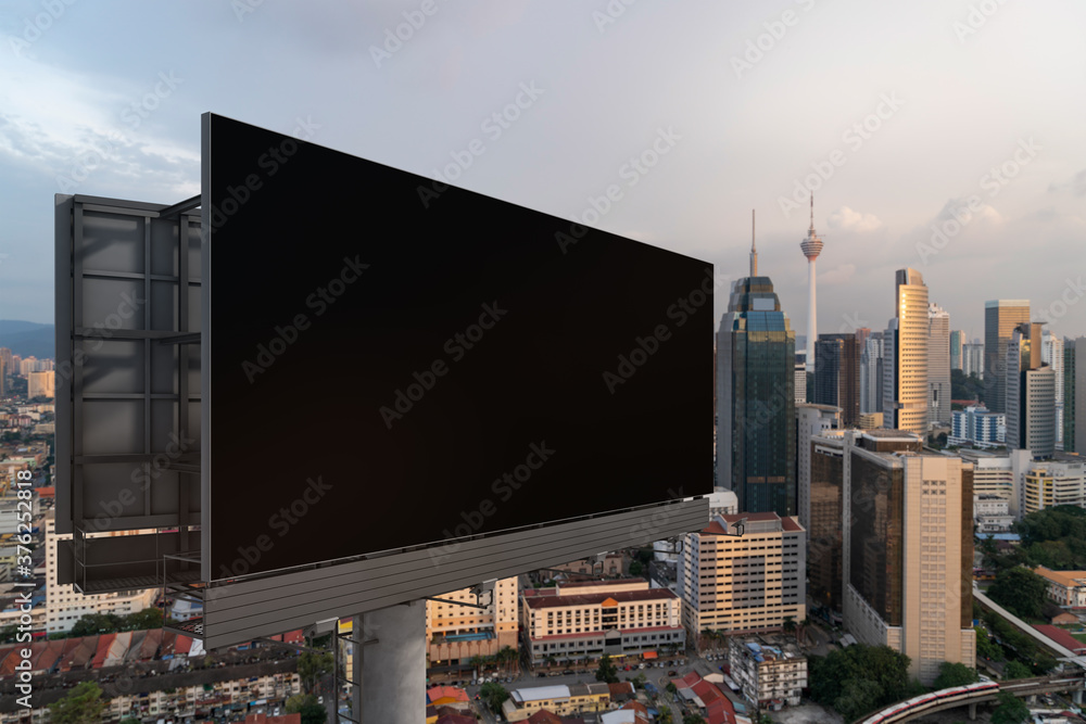 Blank black road billboard with KL cityscape background at sunset. Street advertising poster, mock up, 3D rendering. Side view. The concept of marketing communication to promote or sell idea.