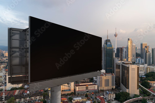 Blank black road billboard with KL cityscape background at sunset. Street advertising poster  mock up  3D rendering. Side view. The concept of marketing communication to promote or sell idea.