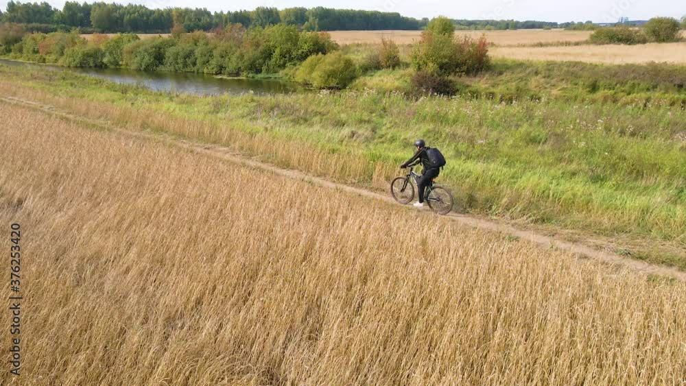 Lone cyclist on a field road near a wheat field - view from a quadcopter Lone cyclist on a field road near a wheat field - view from a quadcopter