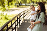 Caring mother with joyful son at the park, beautiful woman hold in arms little boy, mommy gentle looking at the kid, smiling, enjoy family time, motherhood and childhood concept
