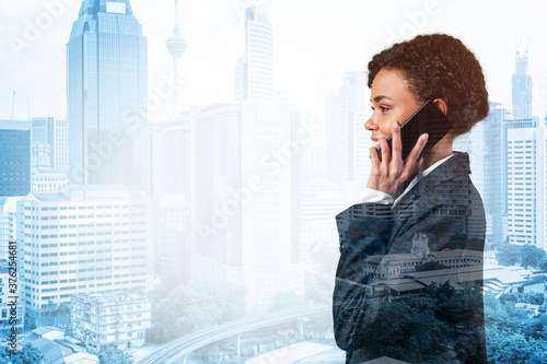 Canvas Print Successful smiling black African American business woman in suit pensively talking phone, Kuala Lumpur cityscape
