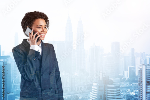 Successful smiling black African American business woman in suit pensively talking phone, Kuala Lumpur cityscape. The concept of consultants as problem solvers. KL skyscrapers. Double exposure. photo