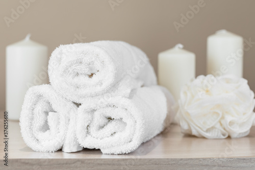 set of white terry towels on a background of candles and a washcloth concept of relaxation bathroom and spa accessories soft focus