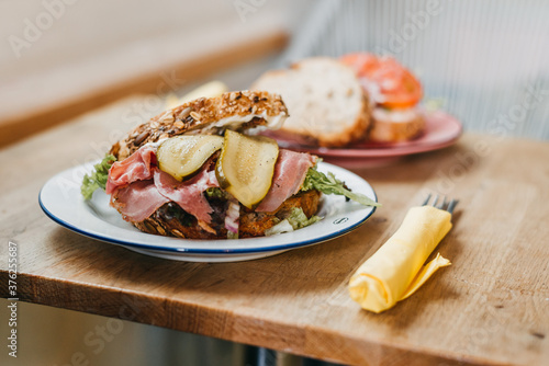 Pastrami Sandwich with pickle and lettuce on a white plate with cutlery next to it