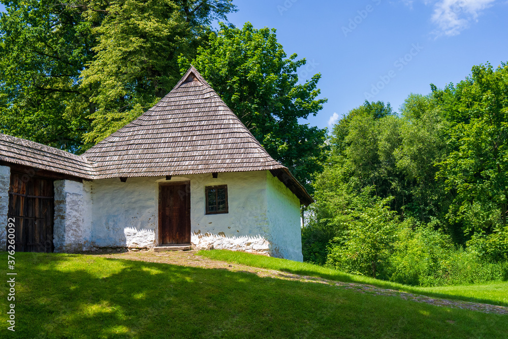 Little stone building with wood shingles roof next to white stone fence with wooden gate. Watchman house uphill. Radruz, Poland, Europe. Little stone building with wood shingles roof next to white stone fence with wooden gate. Watchman house uphill. Radruz, Poland, Europe.