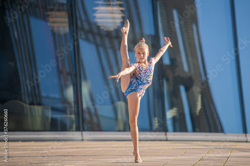 A girl gymnast of school age in a beautiful cross-dress with a black suit performs an exercise without an apparatus.