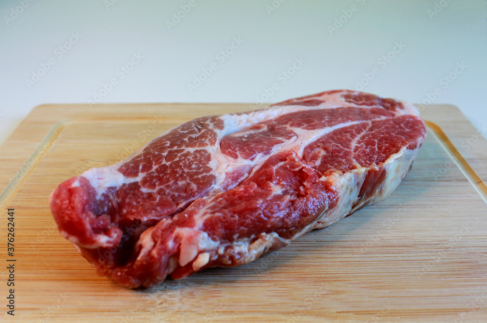 A piece of fresh red meat lying on a cutting board. Pork steak. Selective focus. A piece of fresh red meat lying on a cutting board. Pork steak. Selective focus.