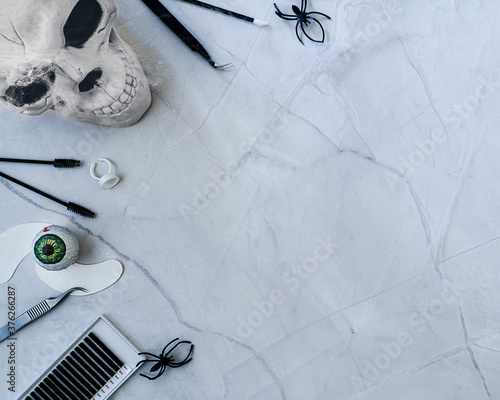 A happy Halloween themed beauty background. Treatment tools and products arranged on left side of frame with spooky accessories include spiders cobwebs   skeleton heads. Flat lay style with copy space