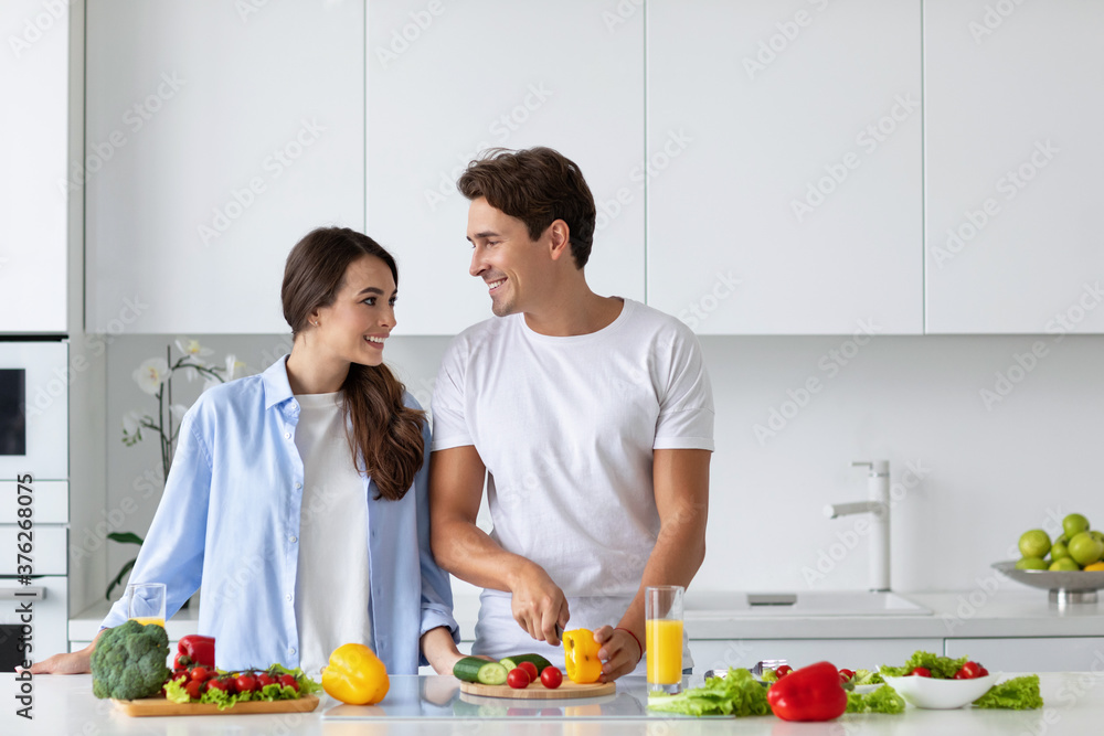 Cute couple cooking in kitchen, man chopping vegetables.