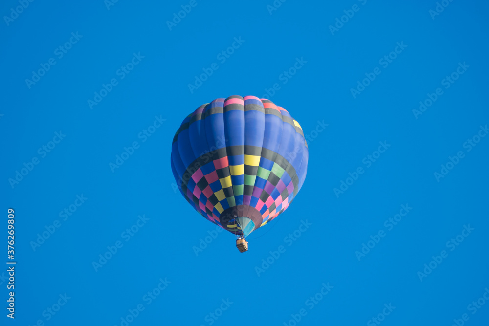 Fototapeta premium Blue patterned hot air balloon rises up overhead on a clear blue sky. Fun adventure tourist activity allows for wonderful views from above.