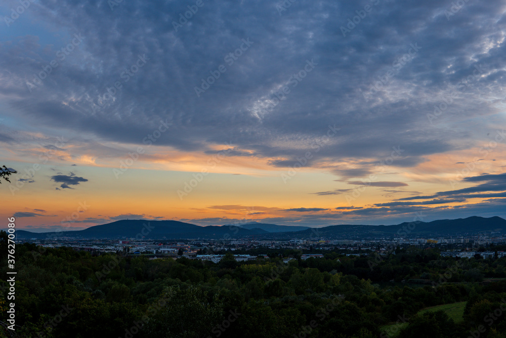 Striking golden sunset over Vienna Austria with a view of the city, green trees, mountains and  gray clouds