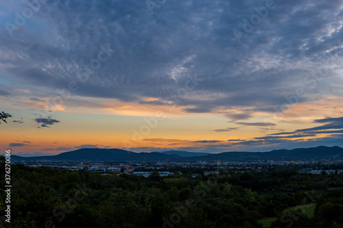 Striking golden sunset over Vienna Austria with a view of the city, green trees, mountains and gray clouds