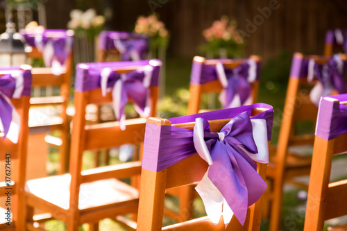 In the photo we see chairs decorated with lavender lilac ribbons. Outdoor wedding ceremony. Lavender-style location prepared.