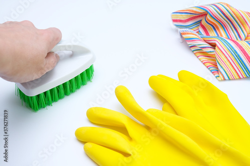 Yellow rubber gloves  microfiber wipe lying on white surface and a hand cleaning it with a brush  housecleaning and housework concept  house hygiene and sanitary protection