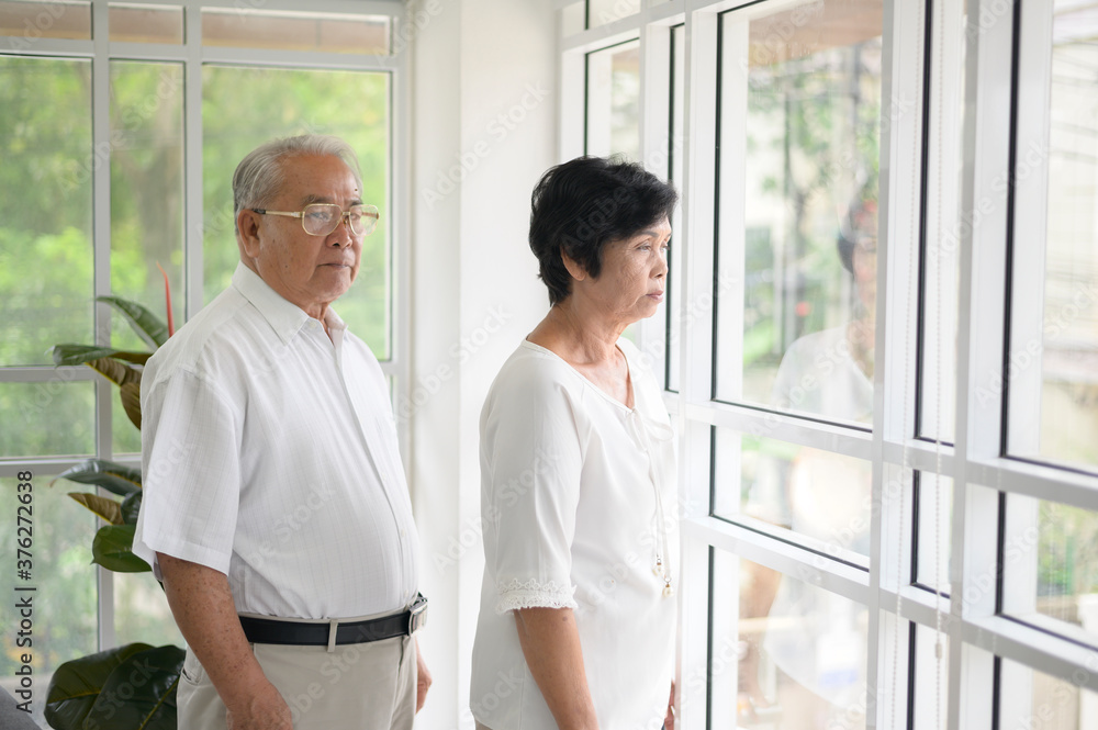 Old couple standing near the window looking outside Old couple standing near the window looking outside