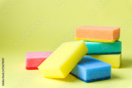 Bright multi-colored cleaning sponges on a yellow background.