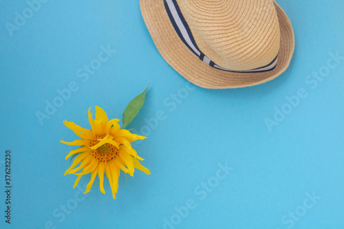 Yellow sunflower and straw hat on a blue background. Copy space. Summer concept.